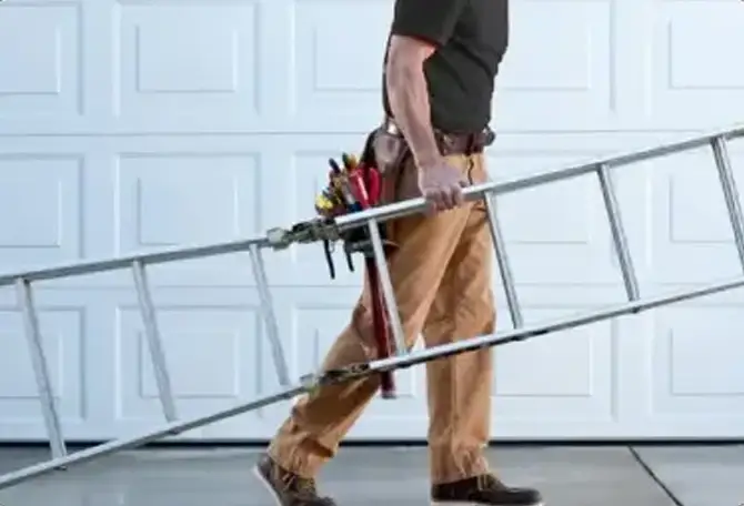 A garage door technician carries a metal ladder in front of a white garage door.